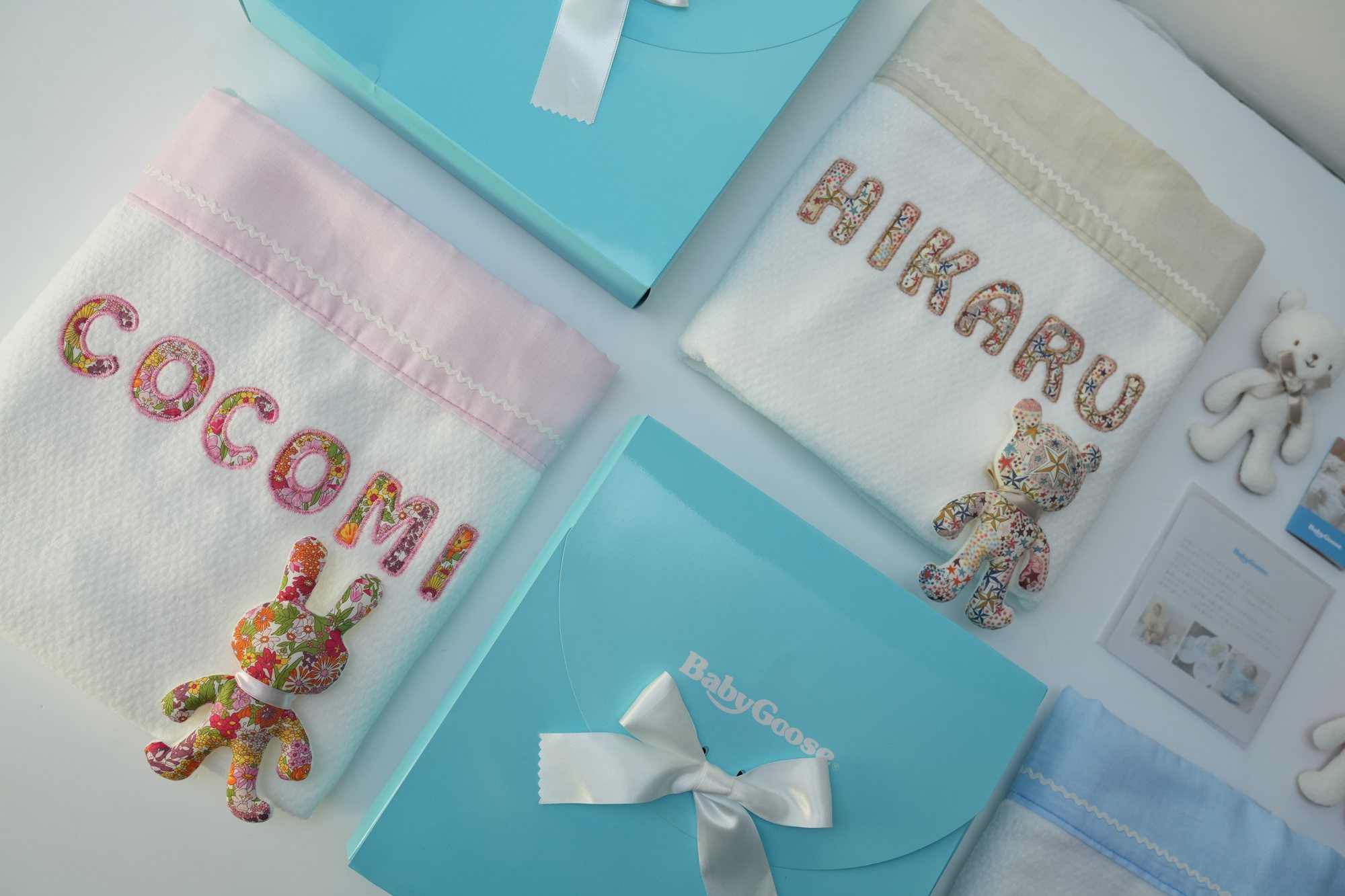 花柄でCOCOMIとうさぎを入れたピンク縁のタオルケットと、HIKARUのタオルケット、水色のギフトボックスを斜めに並べた