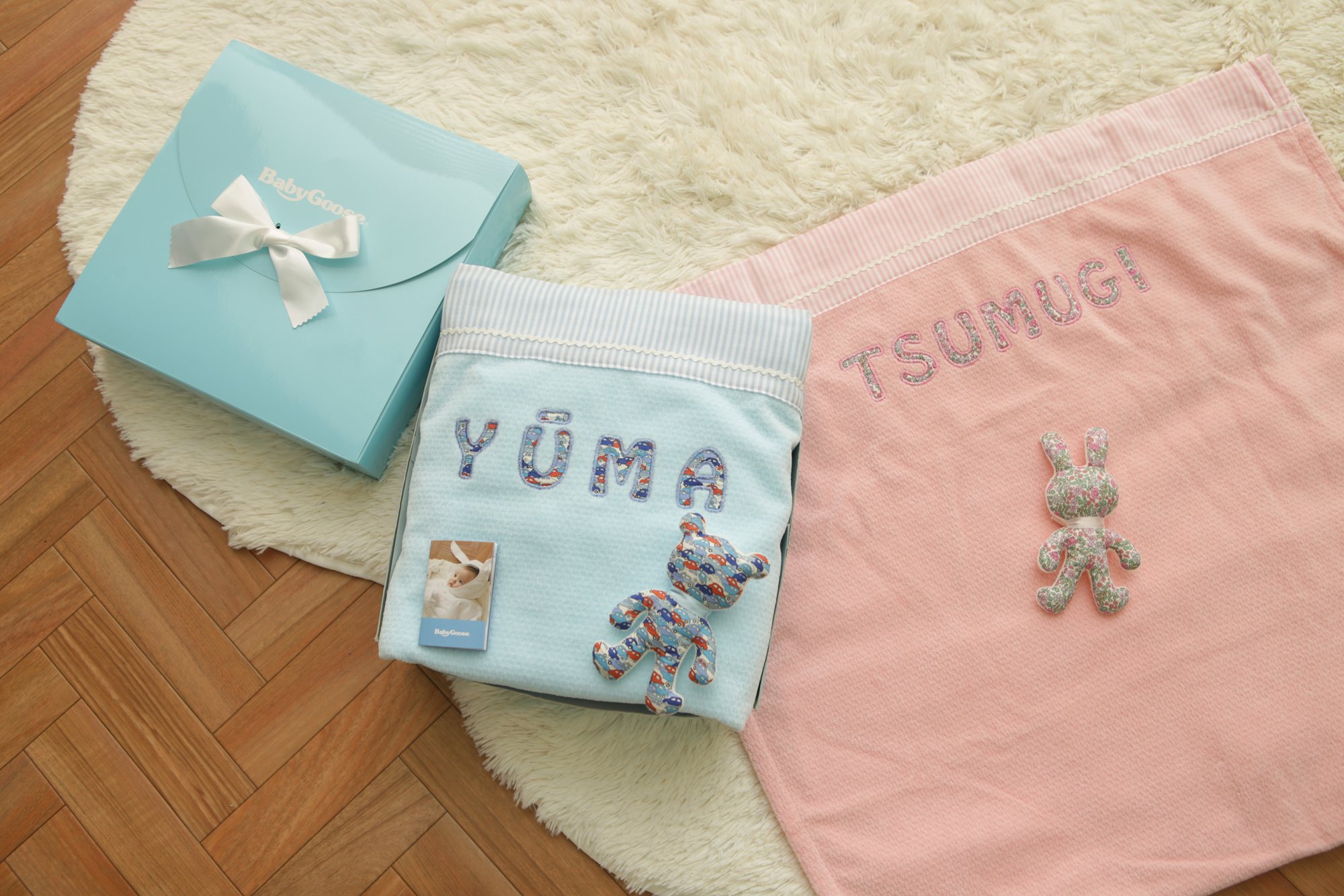 名前刺繍入りの水色とピンクのタオルケットにリバティ柄のくまとうさぎを添え、水色のギフトボックスと並べた様子